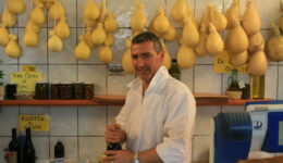 Cheese vendor Costanzo Laprocina with a backdrop of caciocavallo cheese in his shop in Vieste, Puglia