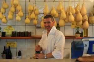 Cheese vendor Costanzo Laprocina with a backdrop of caciocavallo cheese in his shop in Vieste, Puglia