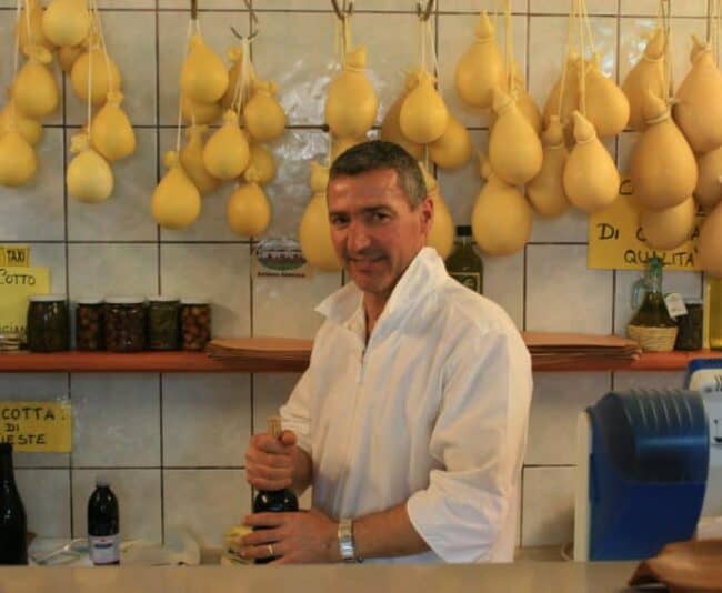 Cheese vendor Costanzo Laprocina with a backdrop of caciocavallo cheese in his shop in Vieste, Puglia