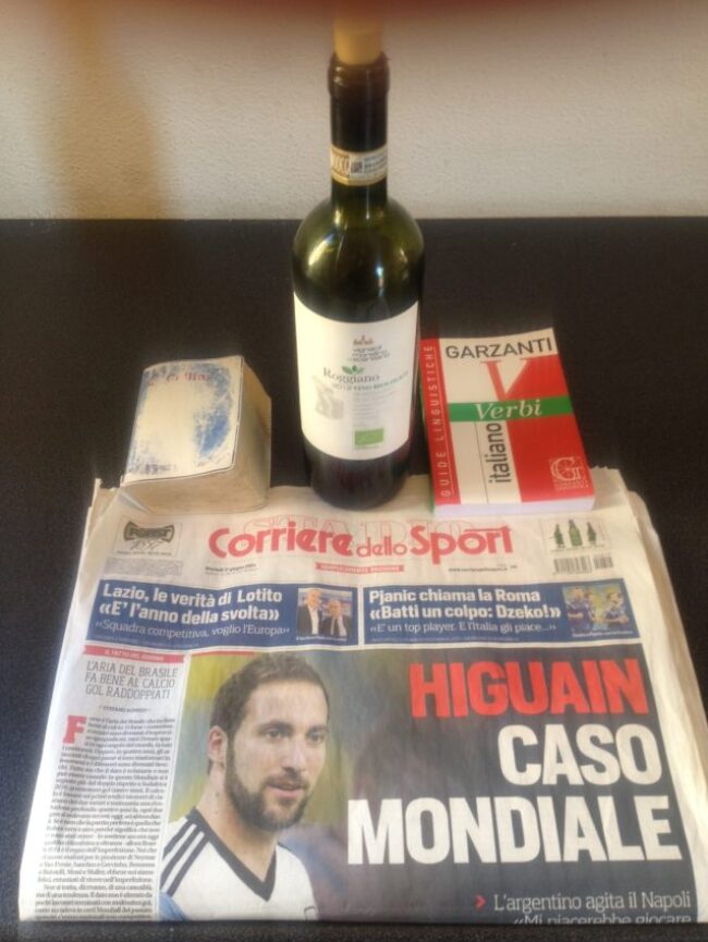The essential tools of learning Italian: an Italian dictionary (notice how well worn), an Italian verb book, an Italian newspaper and the first of many bottles of Italian wine.