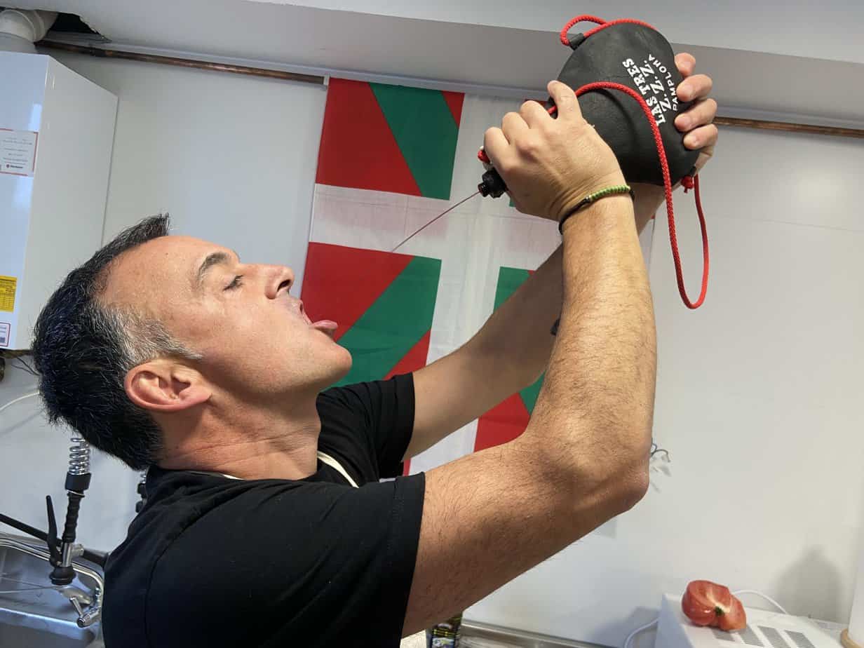 Cook Zigor Egia drinks wine Basque style in front of the Basque flag before our Txoko feast.