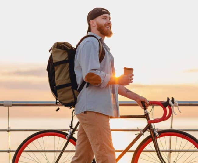 young bearded man traveling on bicycle at sunset sea